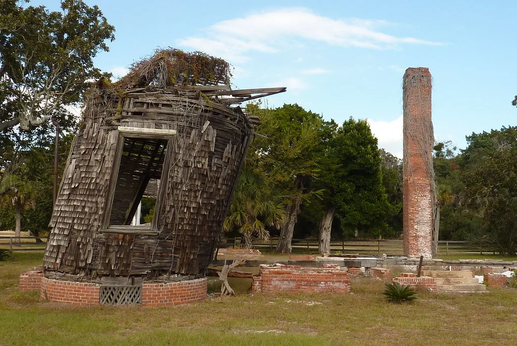 Remains of a house with a leaning wooden turret, brick foundations and an isolated chimney.