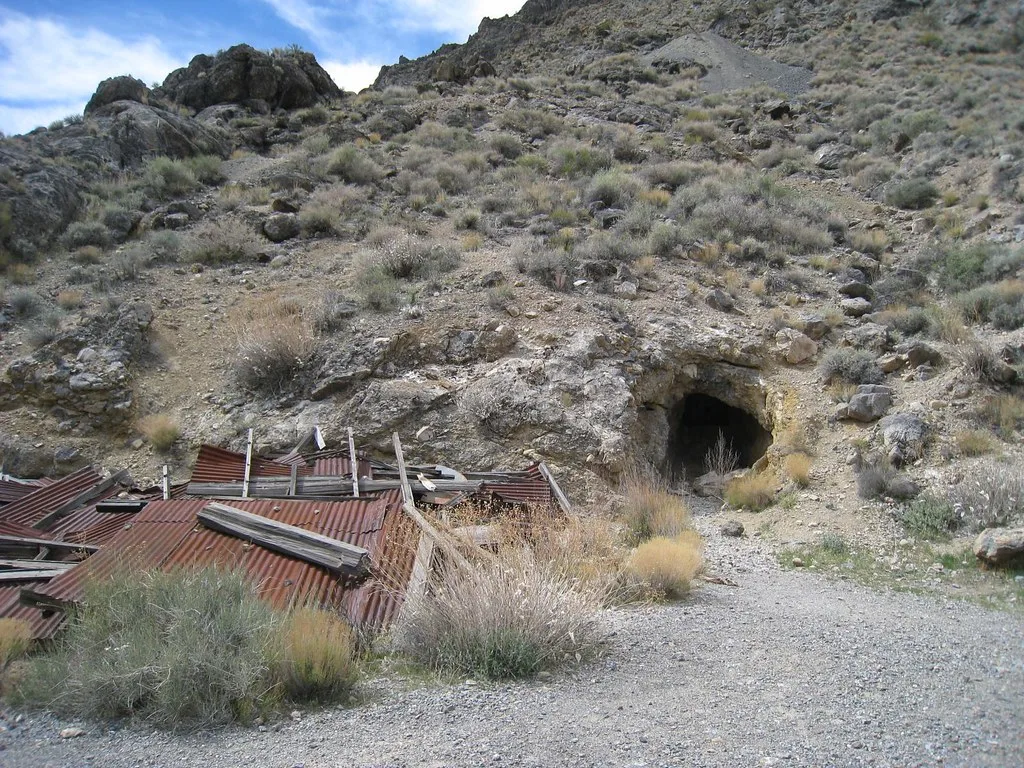 Rock tunnel entrance beside a collapsed sheet-metal structure.