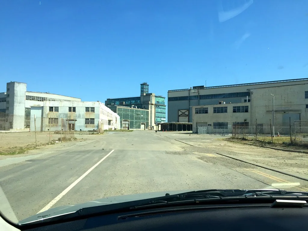 Ensemble industriel désaffecté aux longues façades claires et aux fenêtres brisées.