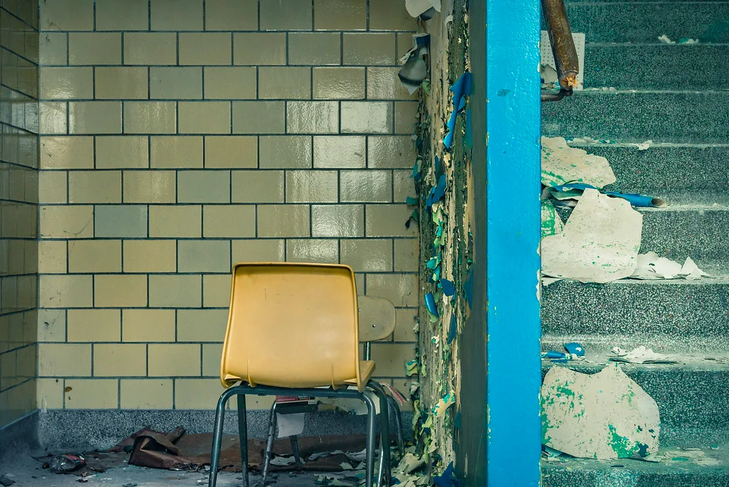 Abandoned landing with a yellow chair before a tiled wall, beside turquoise stairs covered with flakes of paint and plaster.