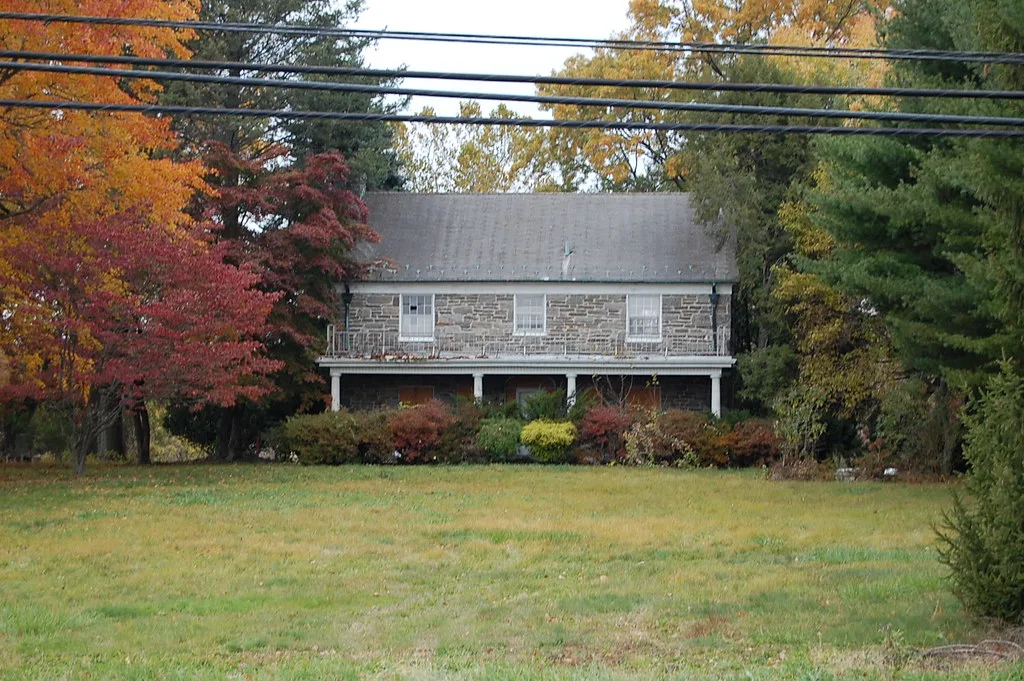 Old stone house with boarded lower openings among autumn trees.