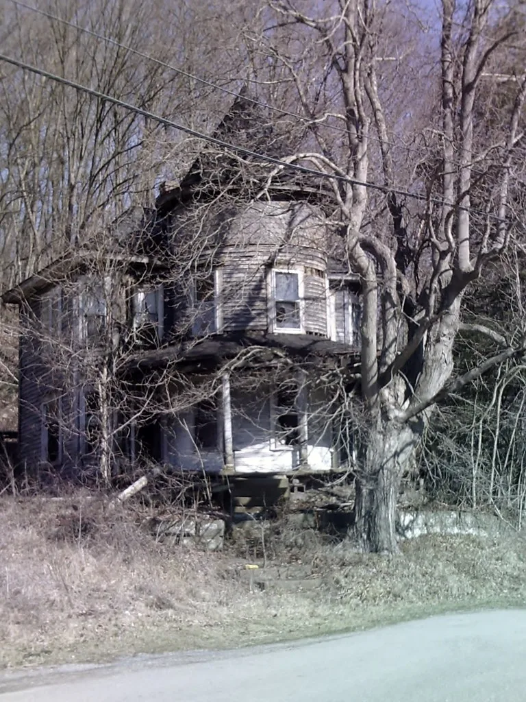 Old wooden house with a turret behind bare trees.