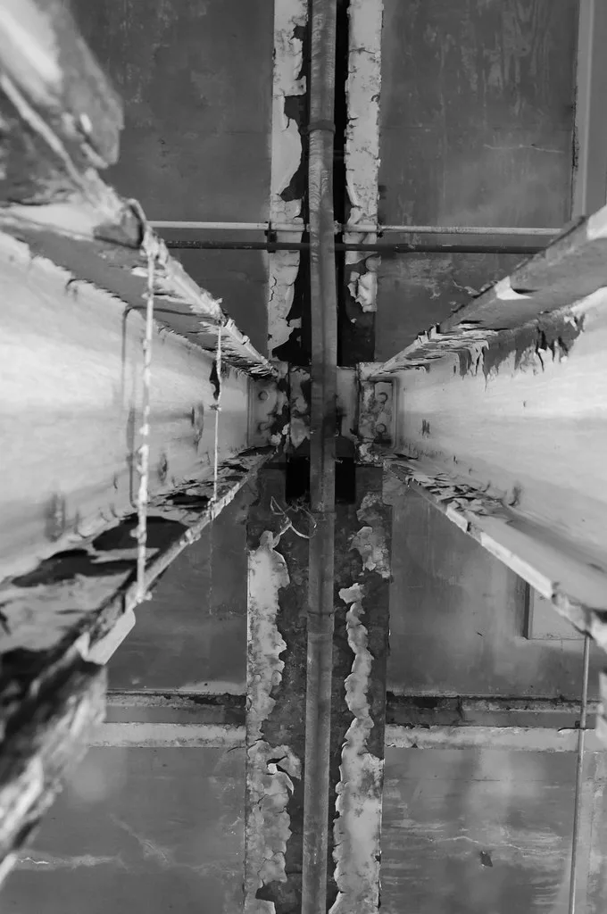 Beams and pipes beneath a ceiling with peeling coatings.