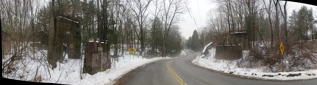 Old bridge abutments on both sides of a snow-lined road.