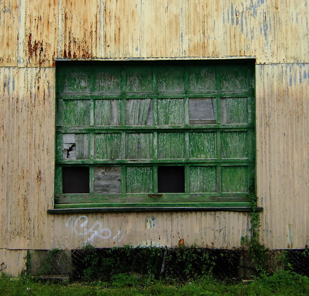 Grande porte verte dégradée dans une façade de tôle rouillée.
