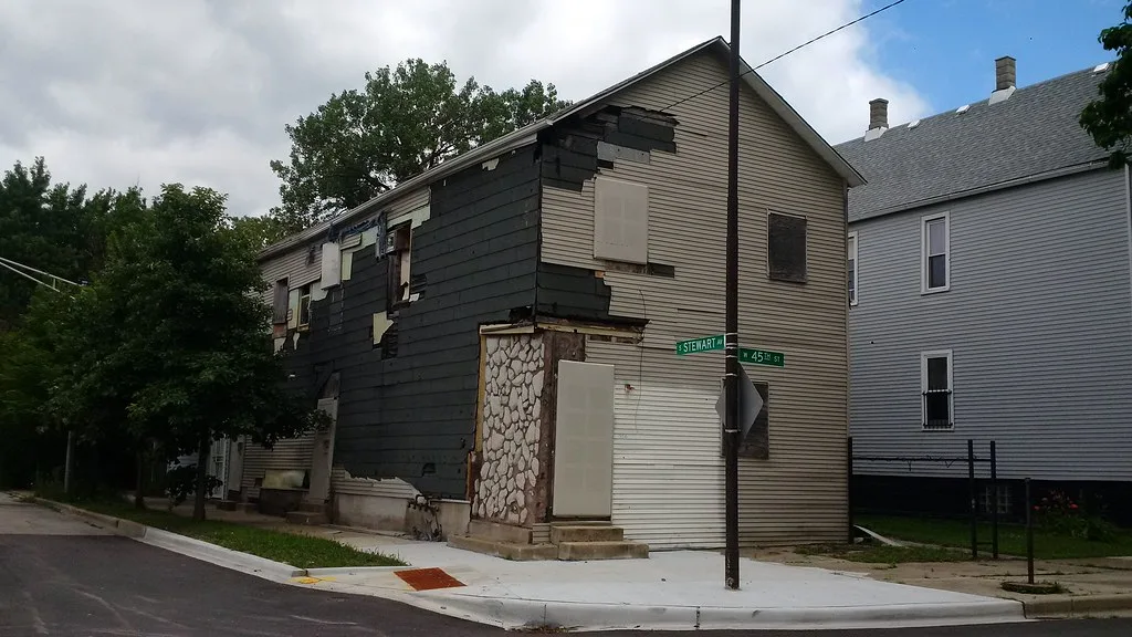 Old corner building with boarded openings and torn-off siding.