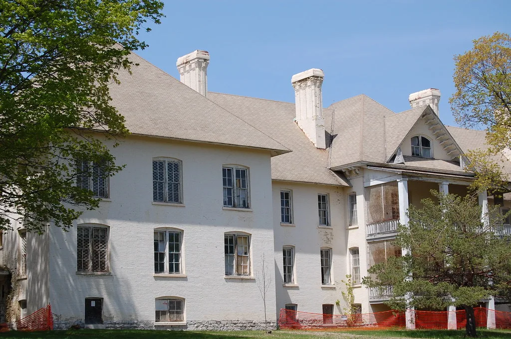 Large white building with brick chimneys, broken windows and screened porches.