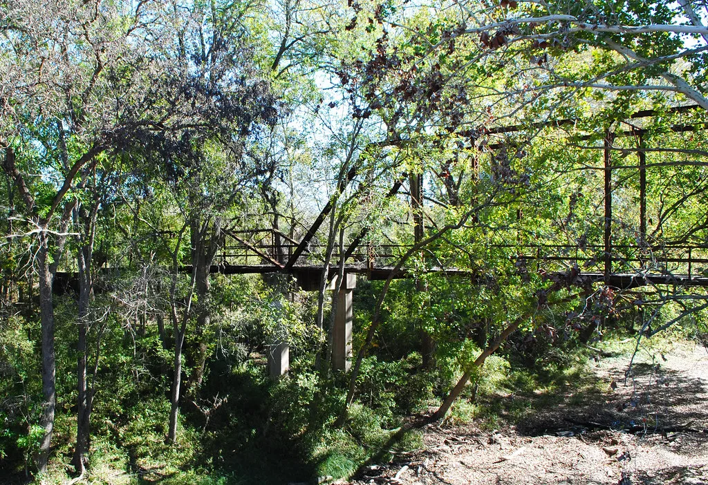 Ancien pont métallique rouillé dont la structure est envahie de branches et de feuillage.