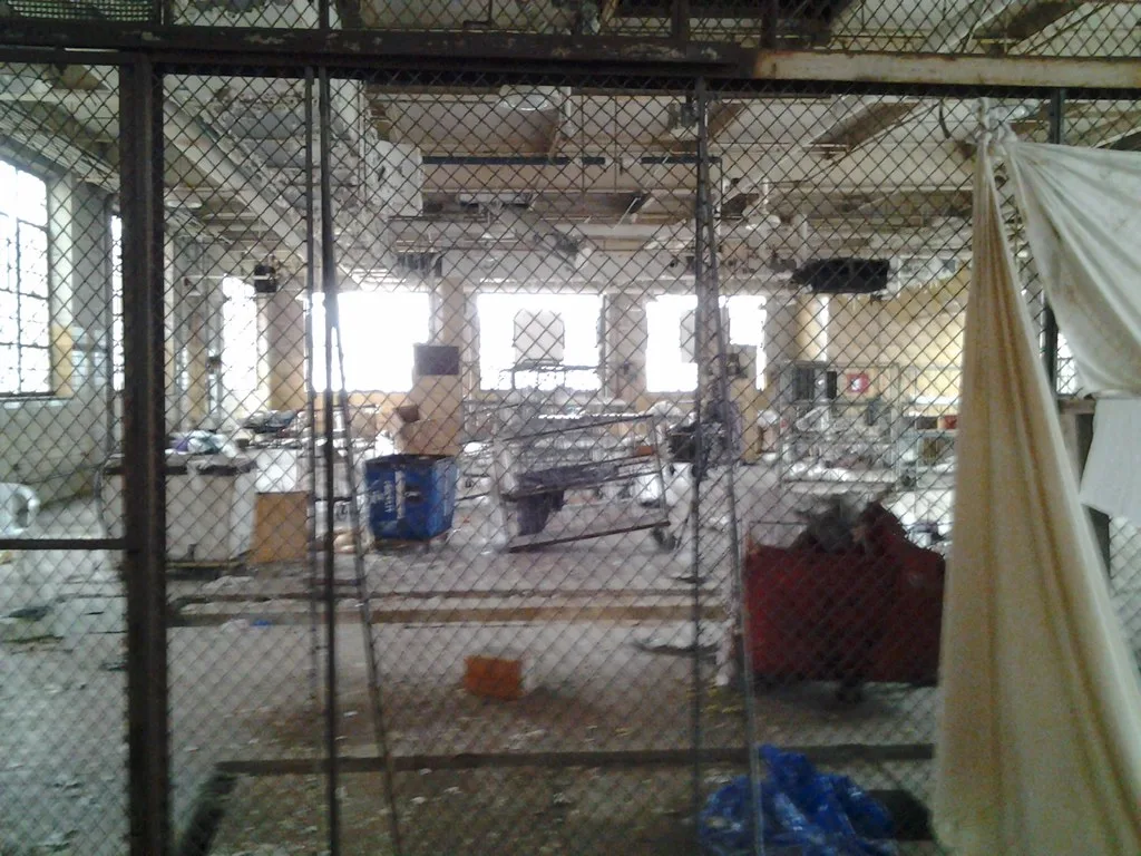 Old industrial room cluttered with equipment behind a wire fence.