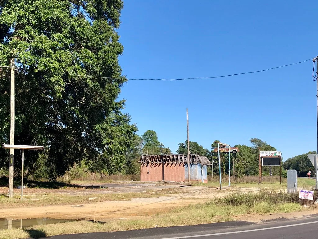 Ancien petit bâtiment à la charpente découverte près d’enseignes routières.