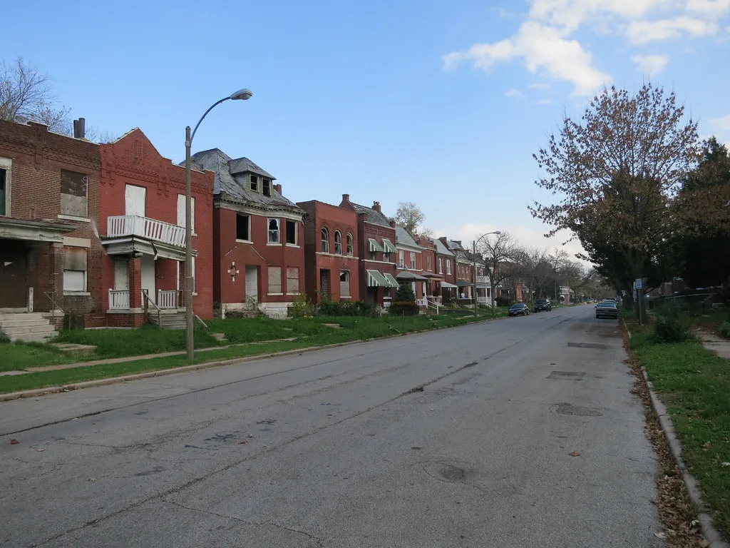Brick houses with boarded openings along a cracked street.