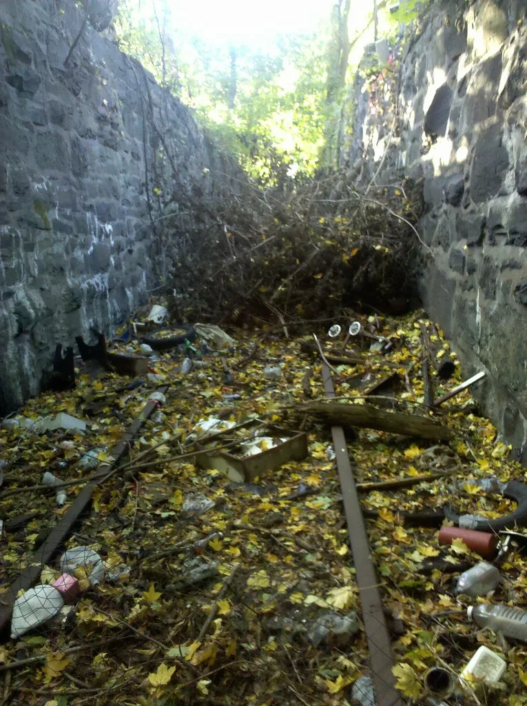 Ruined passage between two stone walls filled with broken timber, litter and leaves.