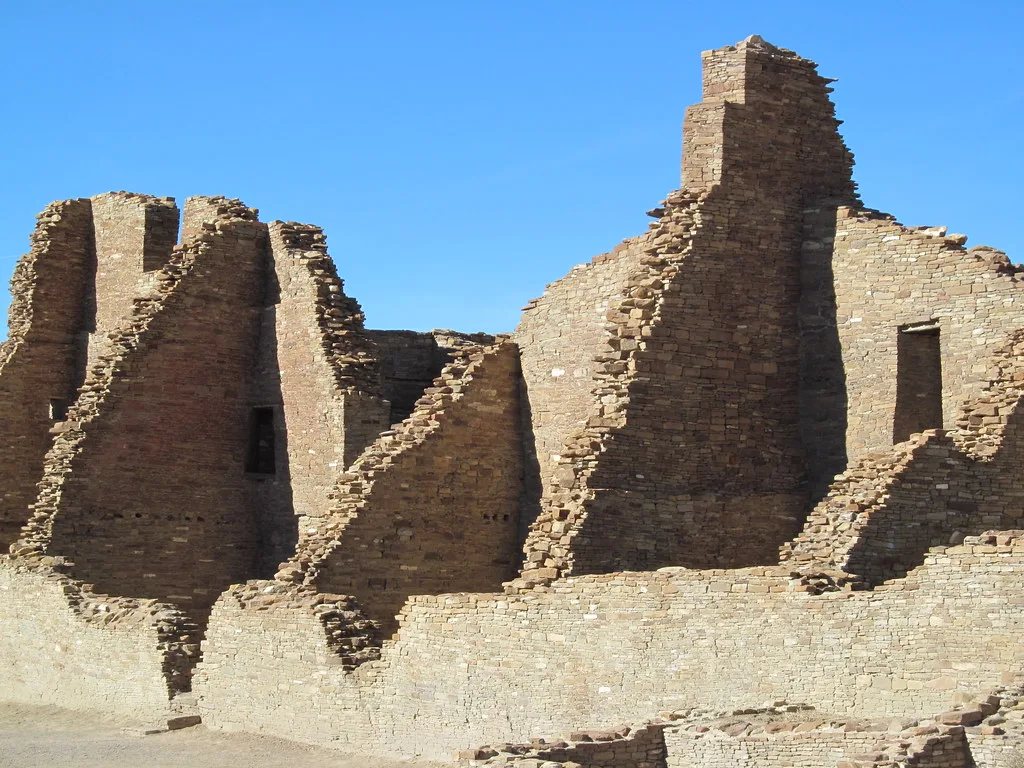 Hauts murs de pierre d’une ruine abandonnée sans toit, aux arêtes effondrées et fenêtres vides sous un ciel bleu.