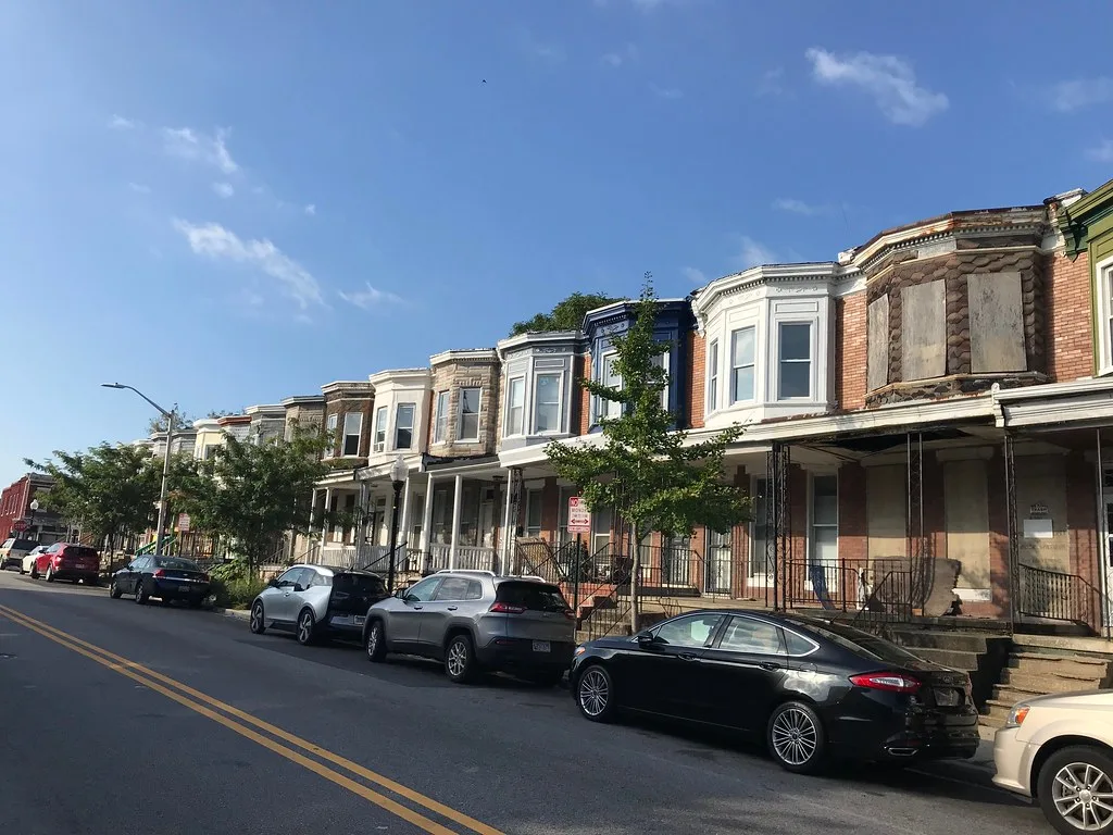 Rowhouses with some boarded openings along a street.