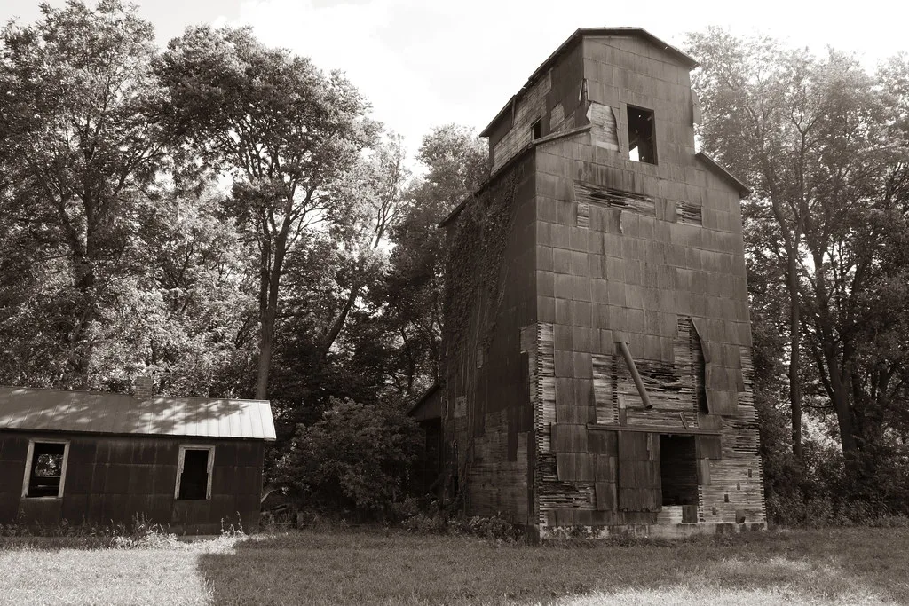 Old tower of wood and torn metal cladding surrounded by trees, in black and white.