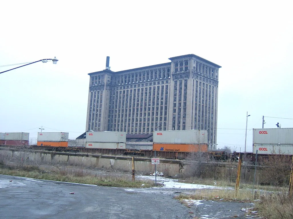 Large deteriorated tower with broken windows behind shipping containers.