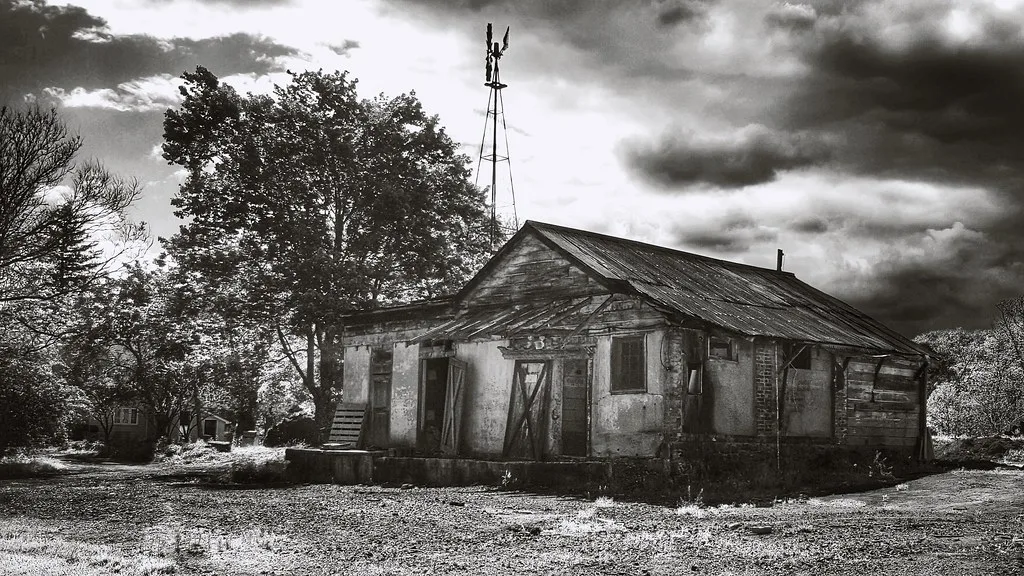 Small building with missing render and boarded doors beneath a weathered metal roof.