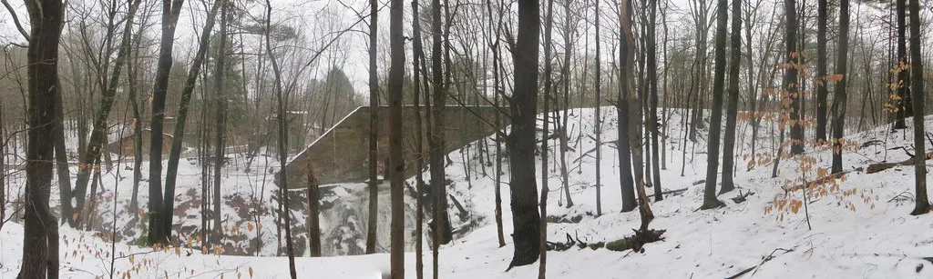 Concrete abutment of a former bridge in a snowy forest.
