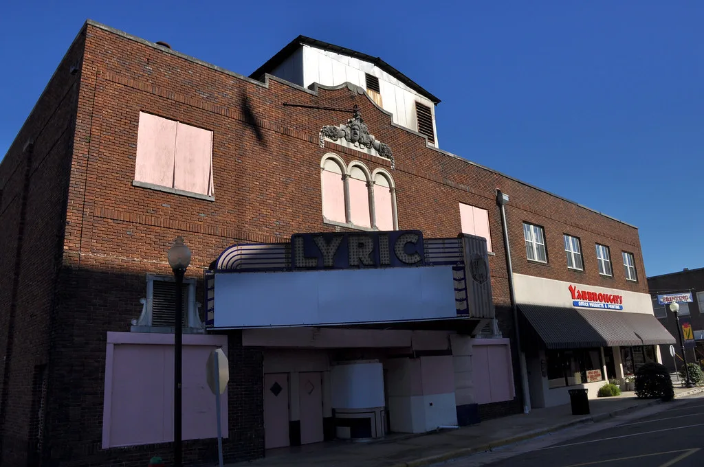 Brick facade of the closed Lyric cinema, with boarded windows and entrances beneath its blank marquee.