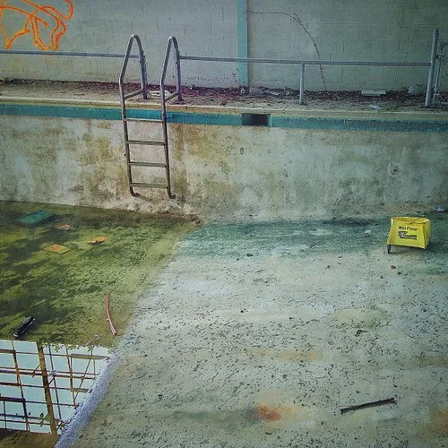Deteriorated old pool with a ladder, debris and standing water.
