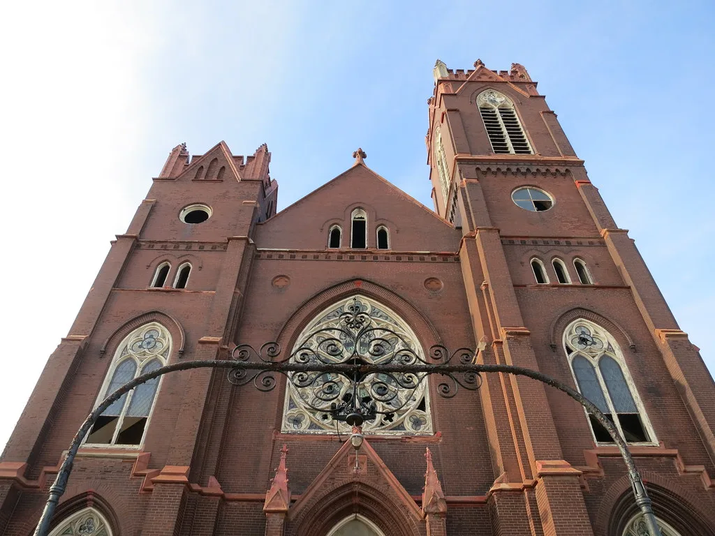 Red brick church facade with broken stained glass and two towers.