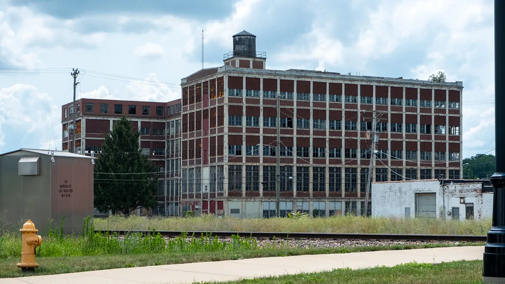 Ancien grand bâtiment industriel rouge et blanc aux fenêtres brisées.