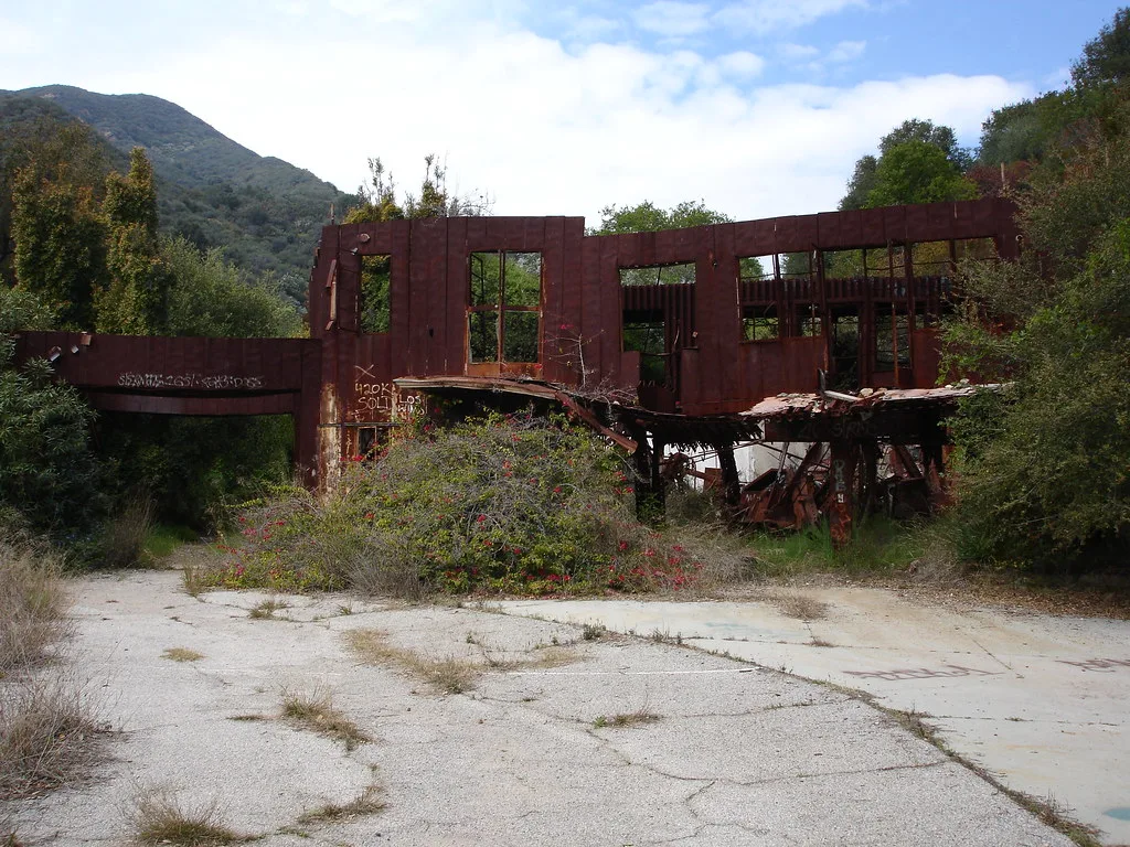 Ruine de bâtiment rouge aux planchers effondrés dans la végétation.