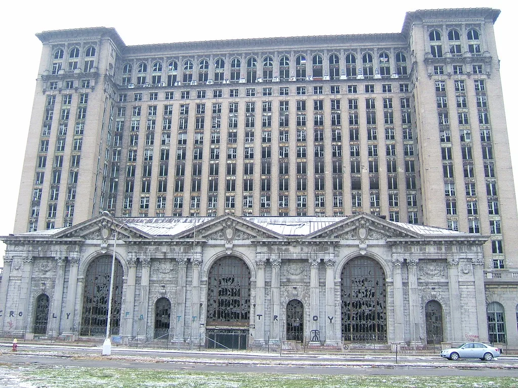 Grand édifice de pierre aux fenêtres brisées derrière une clôture.