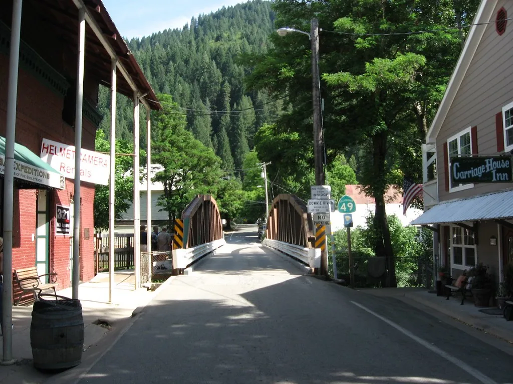 Bridge at the end of a Downieville street, between buildings and a wooded hillside.