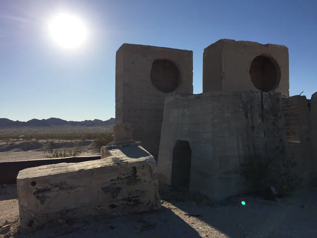 Concrete industrial ruins with two large circular openings in a desert landscape.