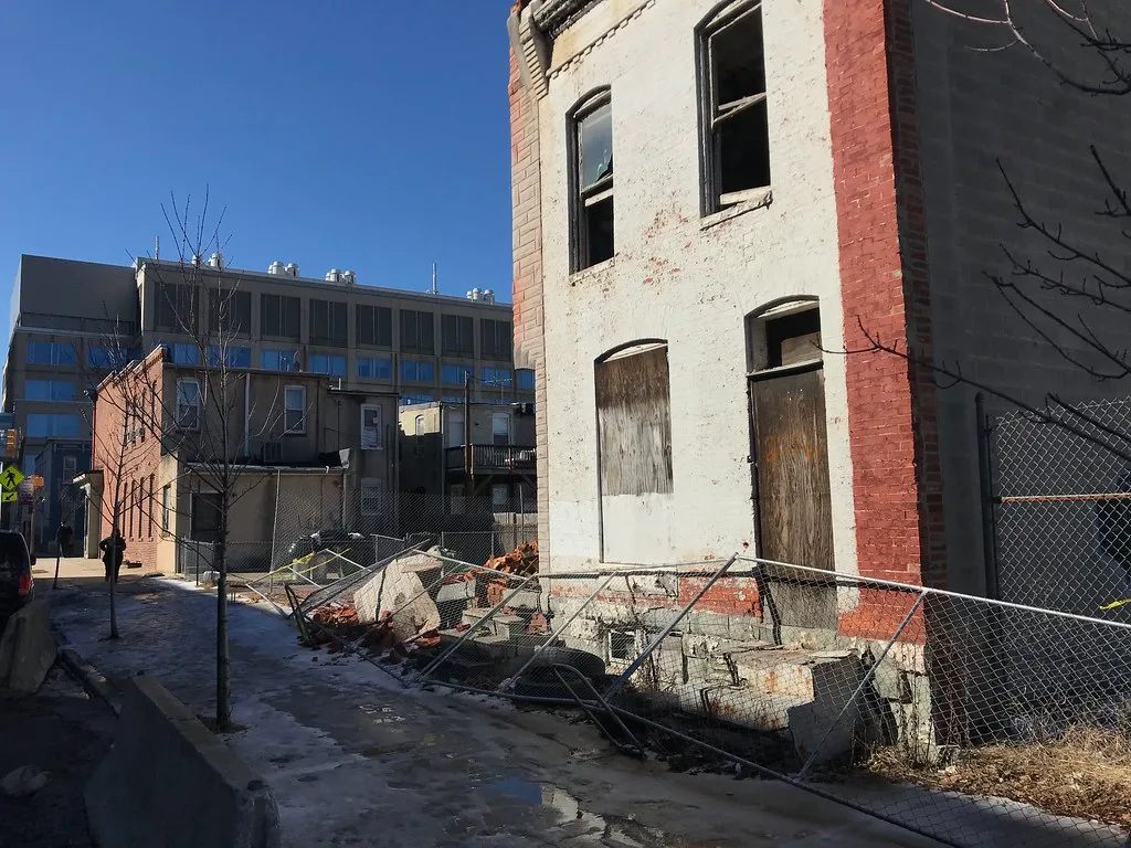 Bâtiment abandonné aux fenêtres brisées au-dessus de gravats et d’une clôture effondrée.