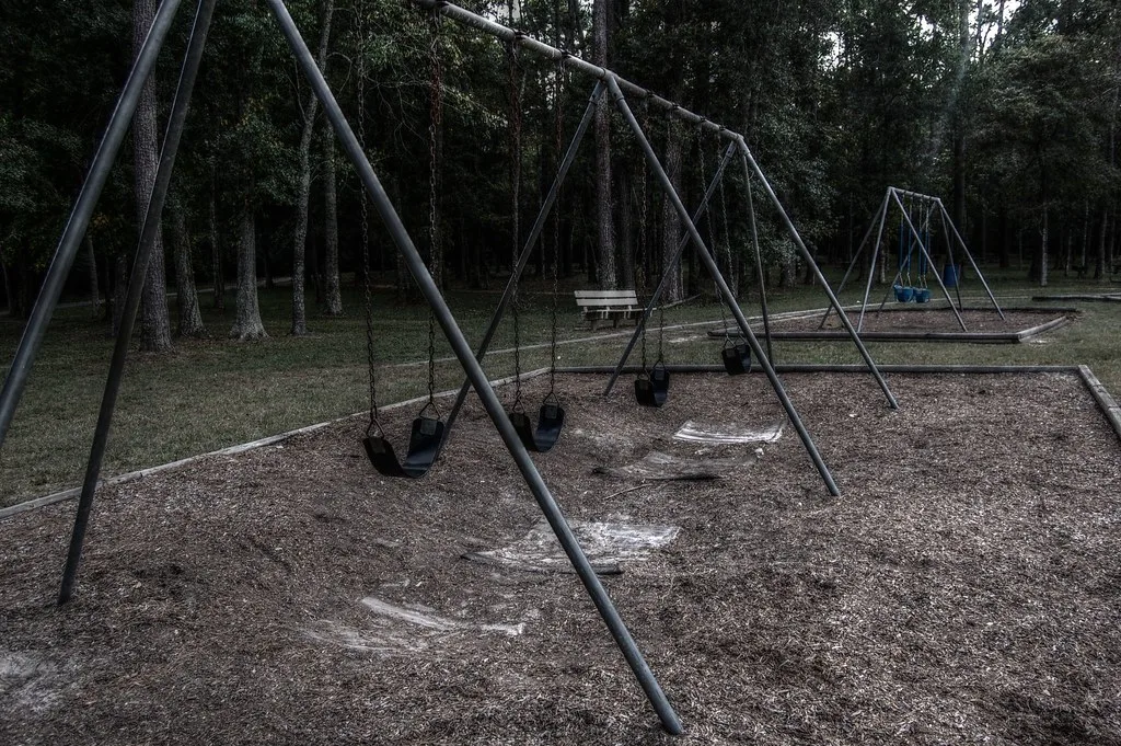 Balançoires vides dans une aire de jeux entourée d'arbres.