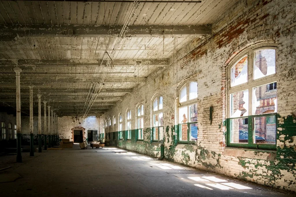 Large industrial hall with broken windows and deteriorated white and green walls.