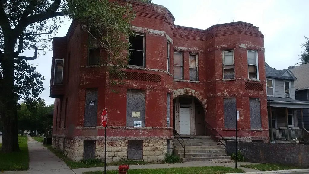 Old red building with boarded and broken windows on a street corner.