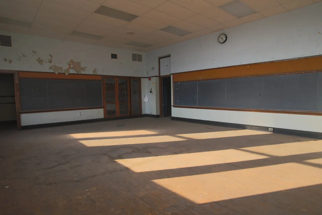 Ancienne salle de classe vide aux murs écaillés et tableaux noirs.