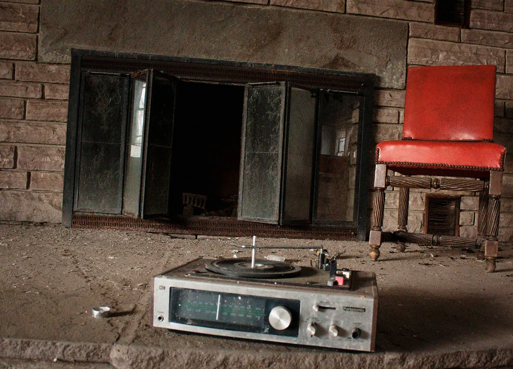 Dusty record player and red chair in front of an old fireplace.