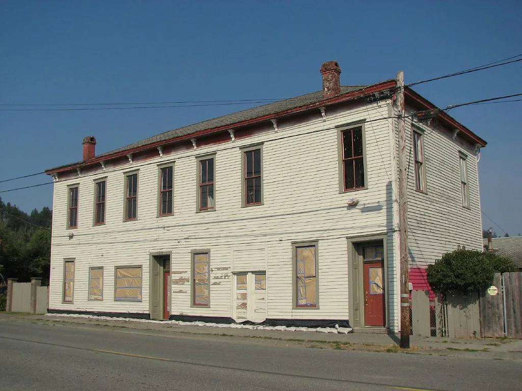 Old white wooden building with covered ground-floor windows.