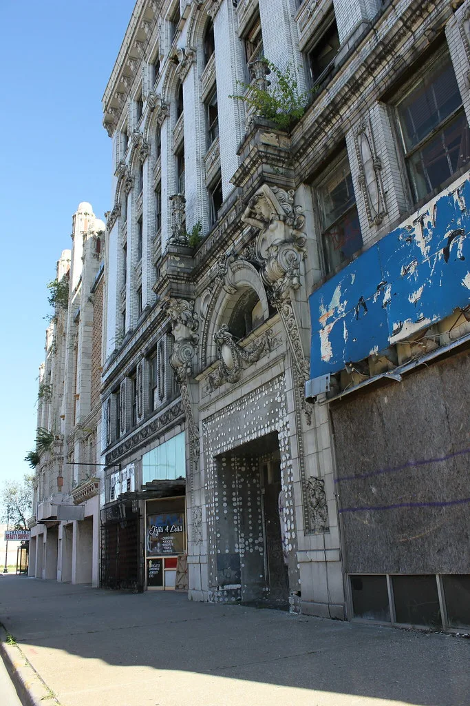 Ornate facade of an old boarded building with vegetation on the cornices.