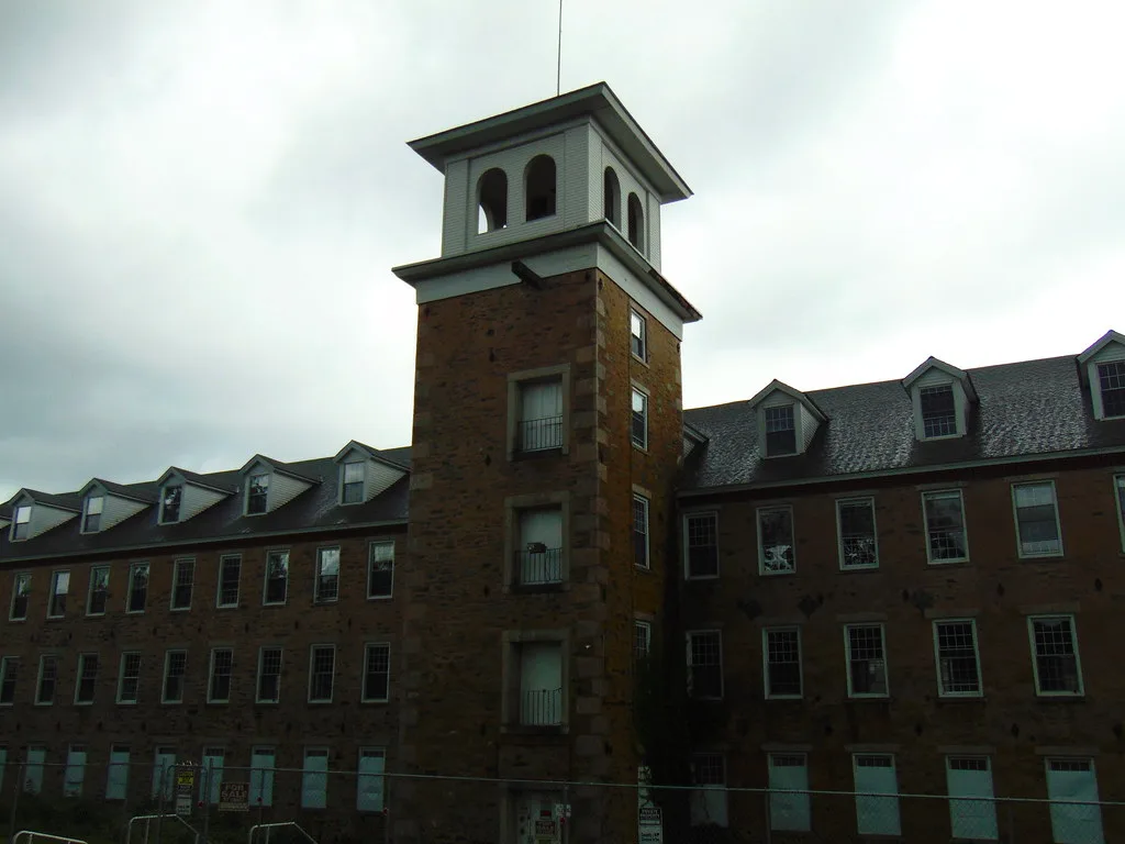 Old stone industrial building with a tower and boarded openings.