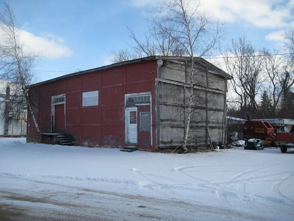 Old red shop with blocked openings in snow.