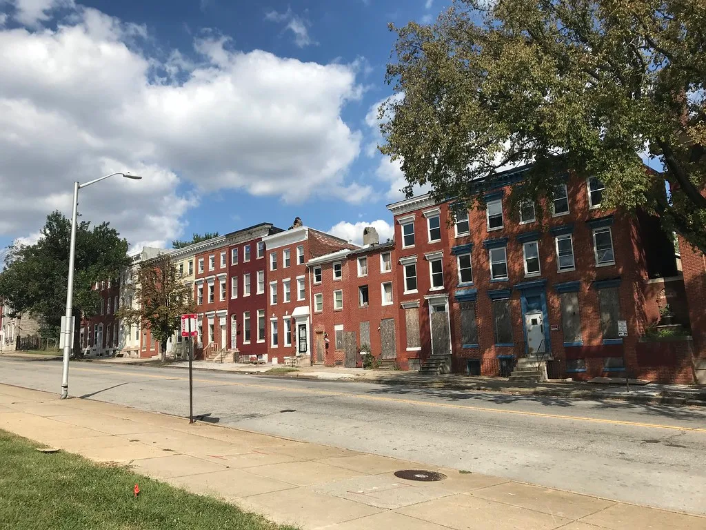 Row of brick houses, several with boarded openings.
