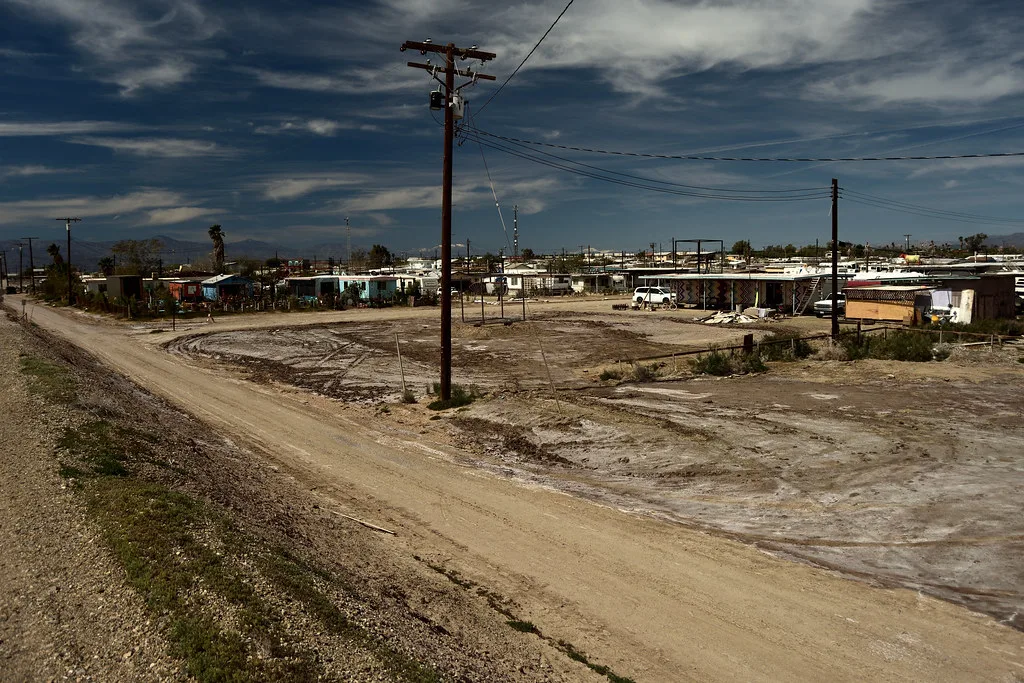 Habitations et terrain vacant à Bombay Beach sous un ciel nuageux.