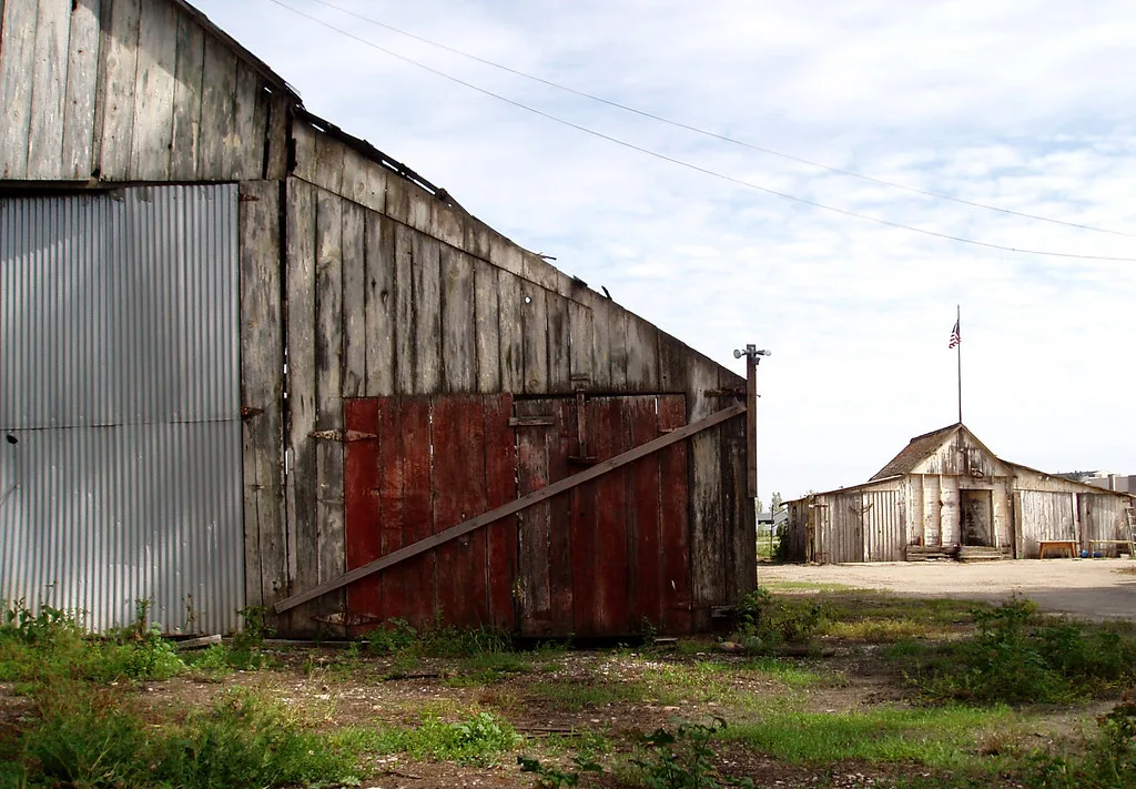 Old wooden sheds with damaged cladding and red doors.