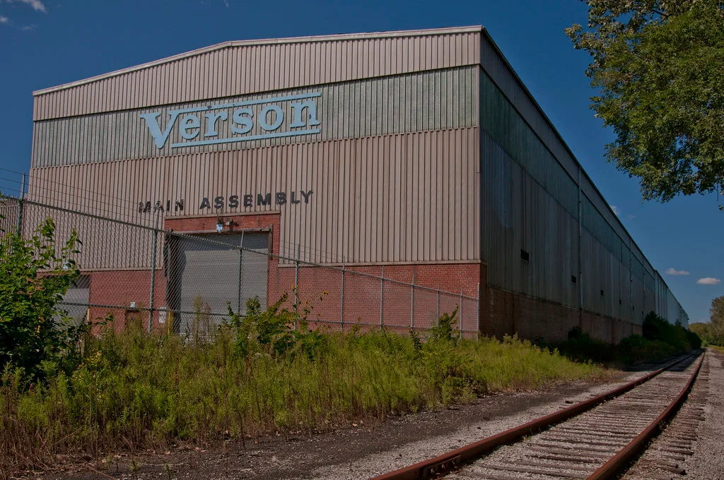 Large closed metal workshop with tall grass along its facade.
