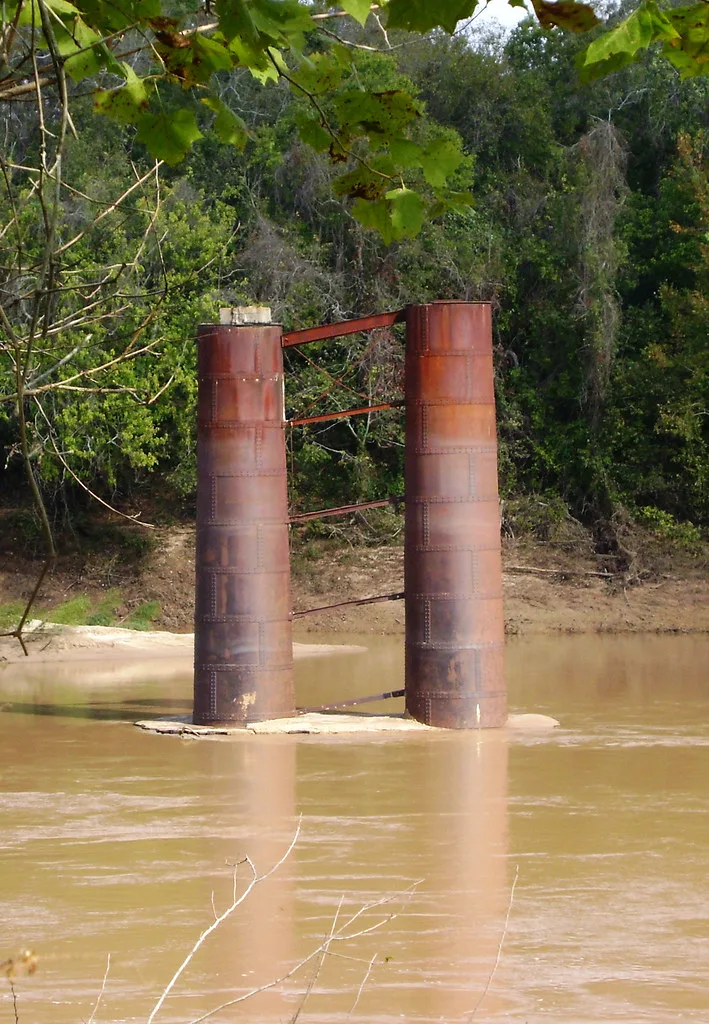Two rusty metal piers standing alone in a river.