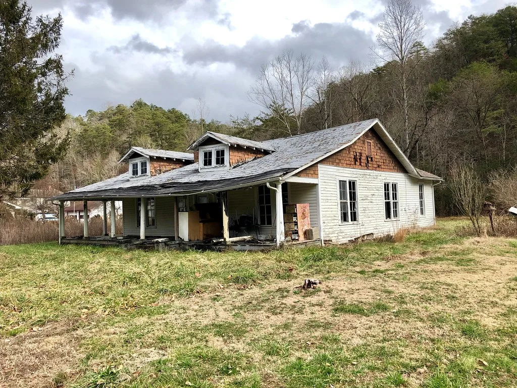 Ancienne maison blanche avec porche dégradé et fenêtres sans vitrage.