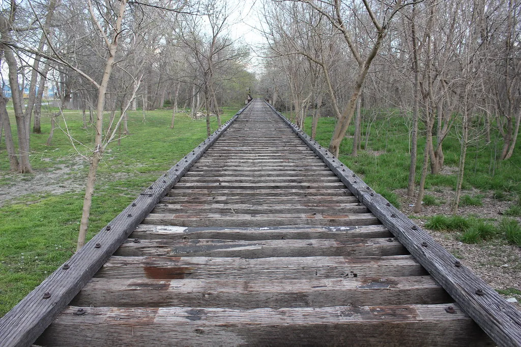 Old wooden railway bridge with its rails removed among trees.