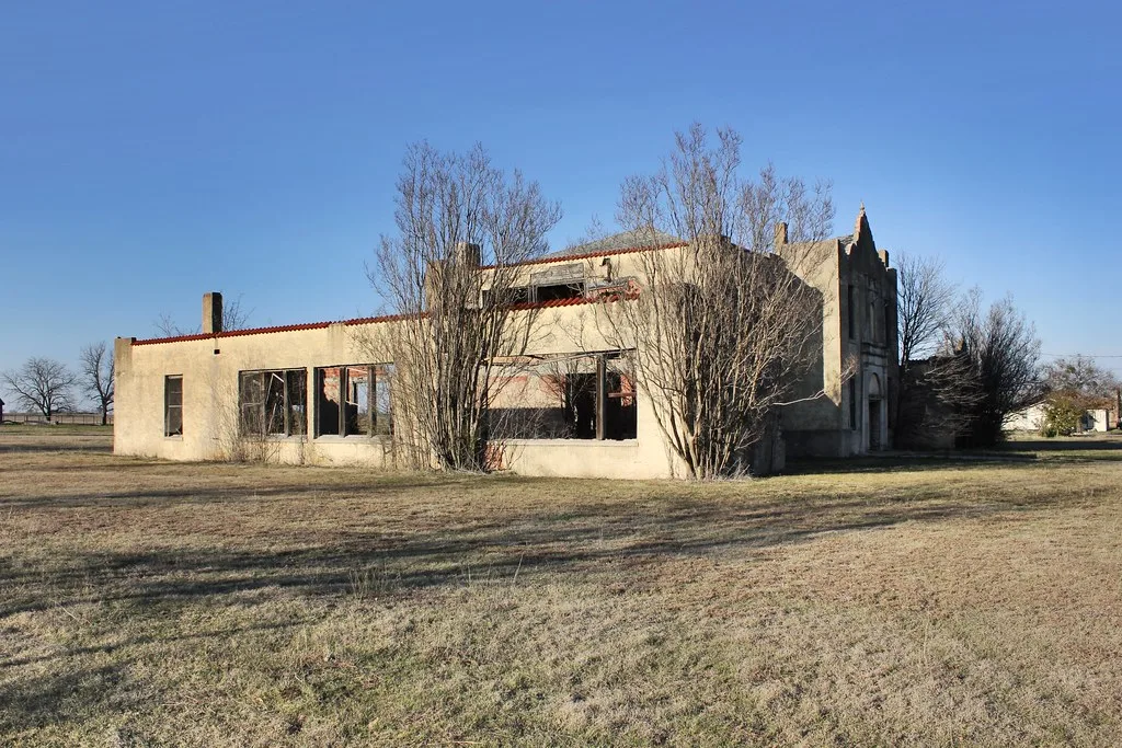 Old pale building with empty windows surrounded by leafless trees.