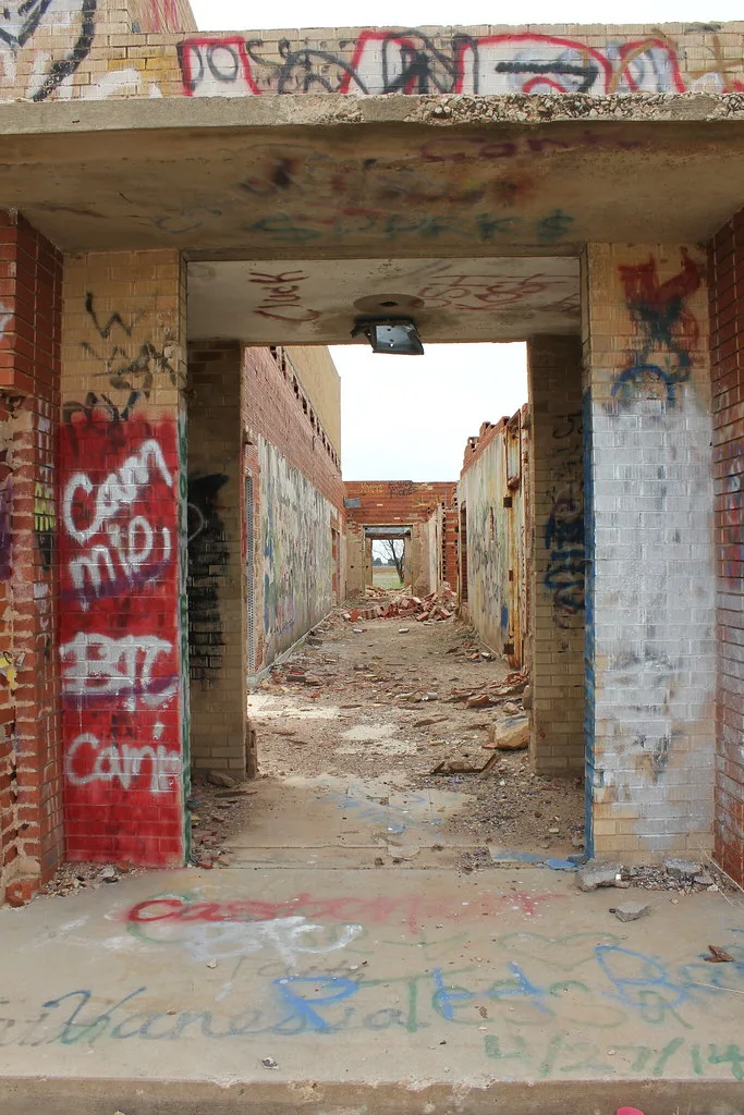 Roofless corridor of a ruined old school with graffiti-covered walls.