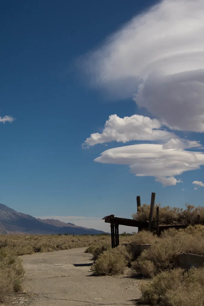 Remains of an old wooden platform in a desert landscape beneath large clouds.